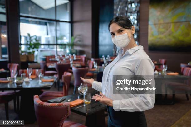 hostess wearing a facemask while welcoming customers at a restaurant - restaurant hostess covid stock pictures, royalty-free photos & images