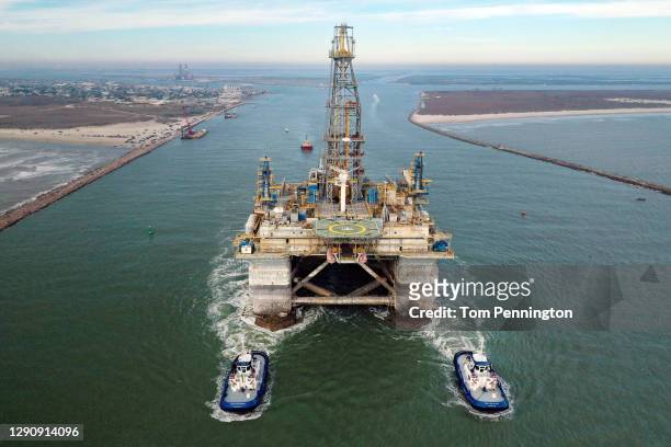 In this aerial image from a drone, tug boats tow the semi-submersible drilling platform Noble Danny Adkins through the Port Aransas Channel into the...