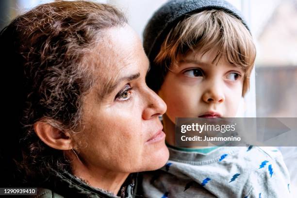 mature woman posing with her son, very sad looking through window worried about loss of her job due covid-19 pandemic - kid looking through window stock pictures, royalty-free photos & images