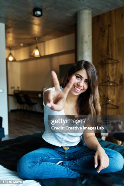 happy young woman gesturing v sign on bed - zwei finger stock-fotos und bilder