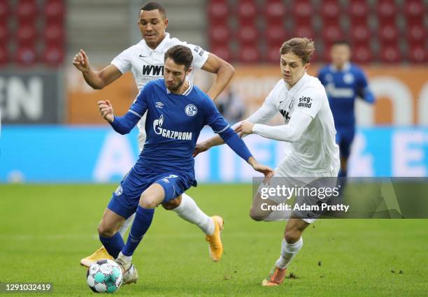 Mark Uth of FC Schalke 04 is put under pressure by Felix Uduokhai and Robert Gumny of Augsburg during the Bundesliga match between FC Augsburg and FC...