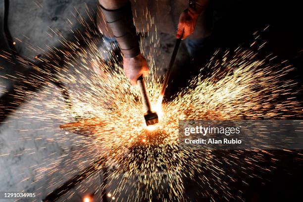 an expert blacksmith works in his workshop, hammering his new creation on his anvil while many sparks fly. - serralheiro imagens e fotografias de stock