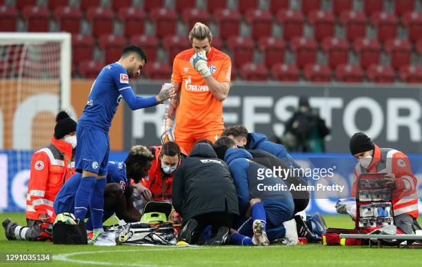 Mark Uth of FC Schalke 04 is checked on by teammates as he receives treatment after a challenge during the Bundesliga match between FC Augsburg and...