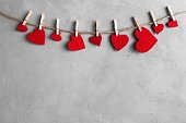 Red hearts on rope with clothespins, on a grey background