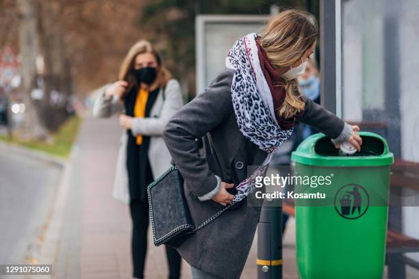 responsible woman throw away her disposable coffee cup at the trash bin while waiting for her bus at the bus station - garbage bin stock pictures, royalty-free photos & images