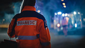 Female EMS Paramedic Proudly Standing With Her Back Turned to Camera in High Visibility Medical Orange Uniform with 