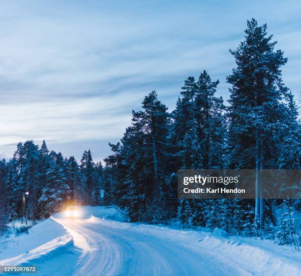 a dusk view of a snow covered fir trees and road, headlights of an approaching car - stock photo - route sapin neige photos et images de collection