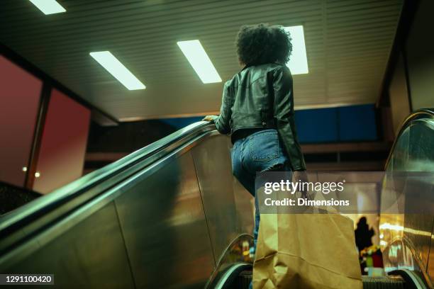 afro-weibchen auf rolltreppe mit einkaufstaschen - metro mall stock-fotos und bilder