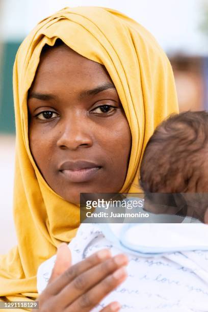 muslim mother holding her baby looking at the camera - refugee babies stock pictures, royalty-free photos & images