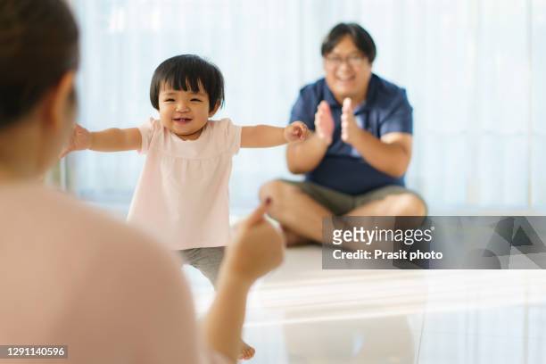 asian girl baby taking first steps walk forward to her mother. happy little baby learning to walk with father help and teaching how to walk gently at home - portrait of young woman standing against steps stock pictures, royalty-free photos & images