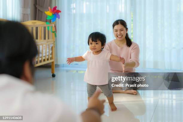 asian girl baby taking first steps walk forward to her father. happy little baby learning to walk with mother help and teaching how to walk gently at home - walking forward stock-fotos und bilder