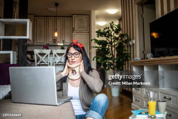 older beautiful black-haired woman after neck injury feels good and spends time in her apartment - woman with cervical surgical collar performs activities at home every day - woman adjusts her collar to tighten the neck - cervical collar stock pictures, royalty-free photos & images