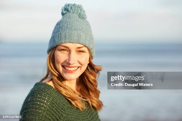 beautiful sunlit woman in bobble hat and wooly jumper on winter beach. - bonnet à pompon photos et images de collection