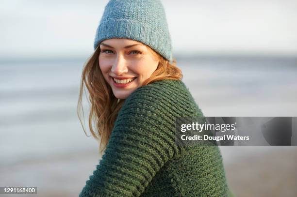 beautiful woman in bobble hat and wooly jumper on winter beach. - beautiful man sunlight stock-fotos und bilder