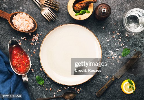 Empty plate and kitchen utensils and ingredients over dark background. Empty plate and kitchen utensils and ingredients over dark background.