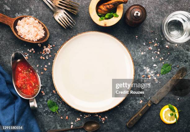 empty plate and kitchen utensils and ingredients over dark background. - empty plate stock pictures, royalty-free photos & images