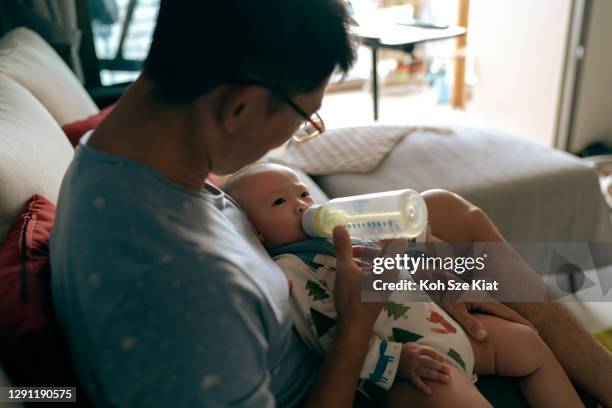 asian father bottle feeding his toddler daughter on a couch - asian baby eating stock pictures, royalty-free photos & images