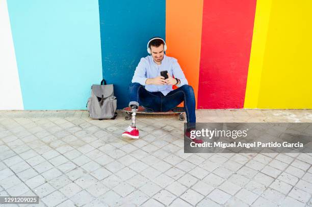 young man with leg prosthesis sitting in the street  using cell phone - 四肢 ストックフォトと画像