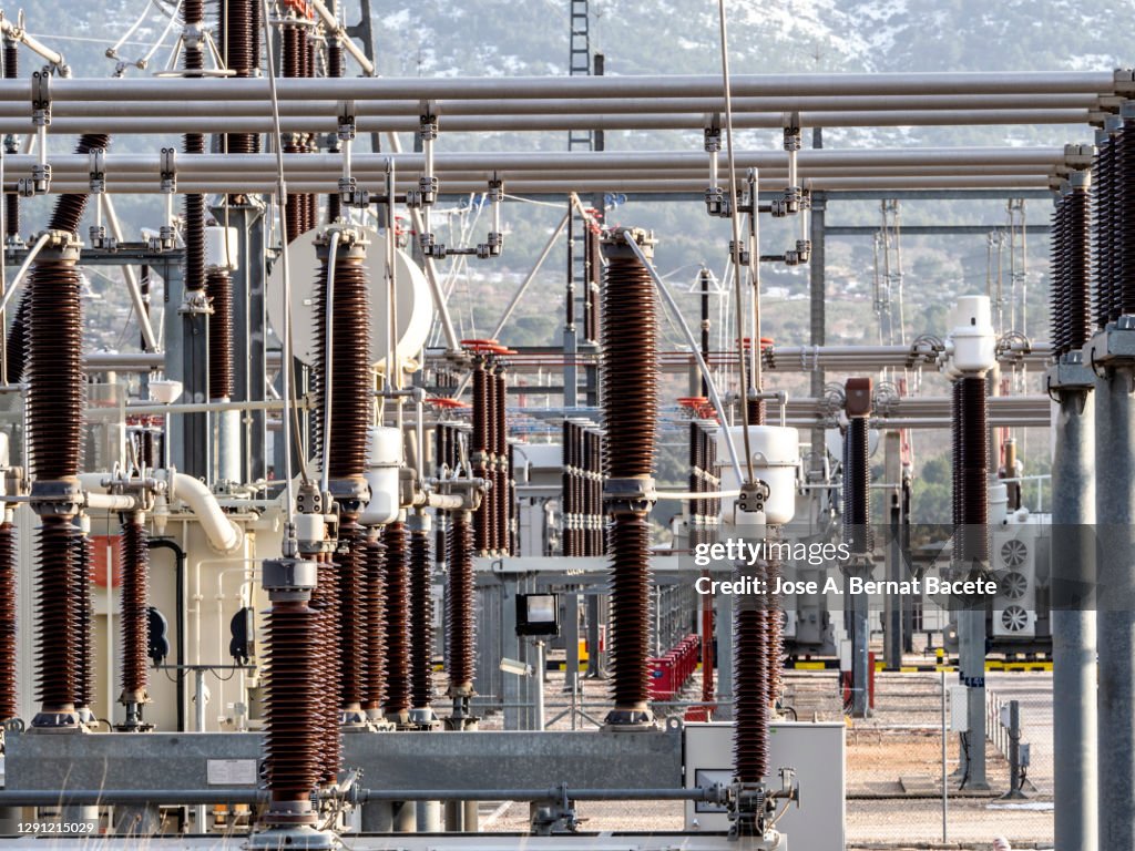 High voltage electric transformer in a power plant in winter with snowy mountains.