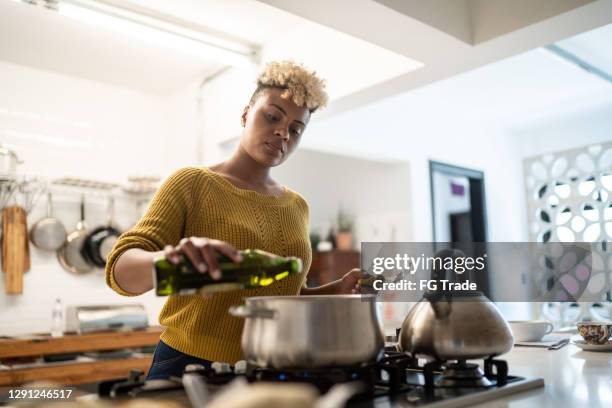 giovane donna che prepara cibo a casa usando l'olio d'oliva - piano del fornello foto e immagini stock