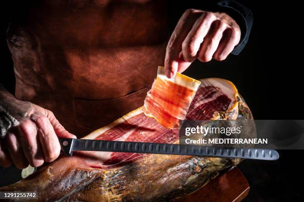 iberian ham serrano ham cutting slice male hands and knife on dark moody - presunto imagens e fotografias de stock