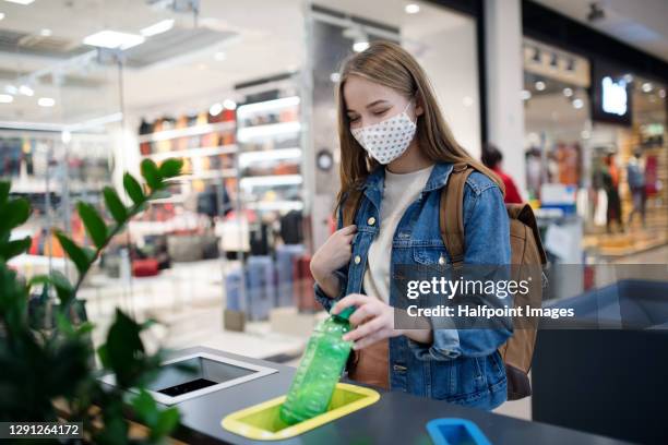 young woman separating waste in bin indoors in shopping center at christmas, coronavirus concept. - stoffbeutel stock-fotos und bilder