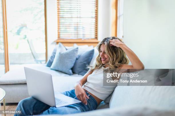 young woman on sofa with laptop - stralende lach stockfoto's en -beelden