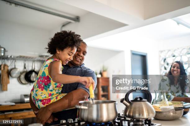 mädchen in den armen des vaters hilft ihm beim kochen zu hause - kids cooking stock-fotos und bilder