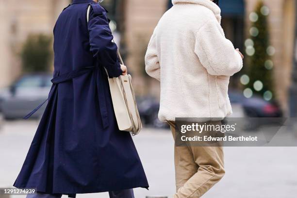 Passerby wears blue long trench coat, a Jacquemus bag ; a passerby wears a white fluffy coat, beige pants, on December 13, 2020 in Paris, France.