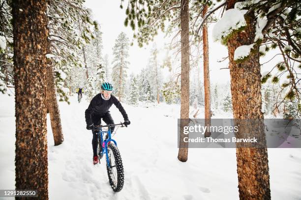 Female cyclists riding fat tire bikes through snowy forest on winter afternoon