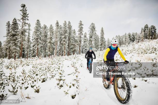 smiling female friends riding fat tire bikes on snow covered trail - wintersport foto e immagini stock