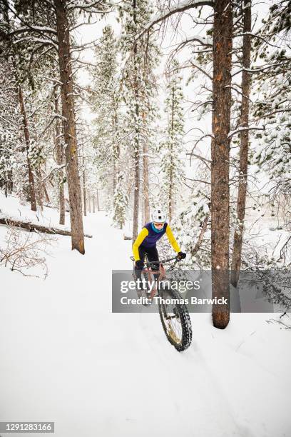 Female cyclist riding fat tire bike through snow covered forest trail