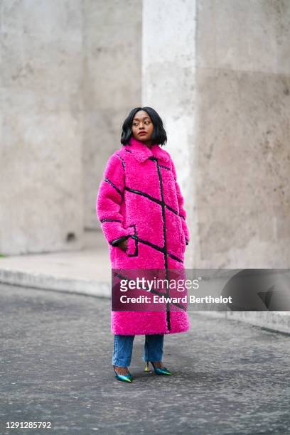 Carrole Sagba wears a neon pink faux fur fluffy winter long coat with black leather stripes from Stand Studio, Zara blue jeans, shiny glittering neon...