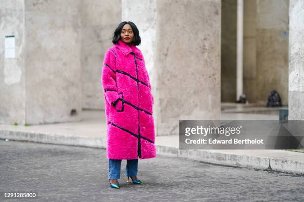 Carrole Sagba wears a neon pink faux fur fluffy winter long coat with black leather stripes from Stand Studio, Zara blue jeans, shiny glittering neon...