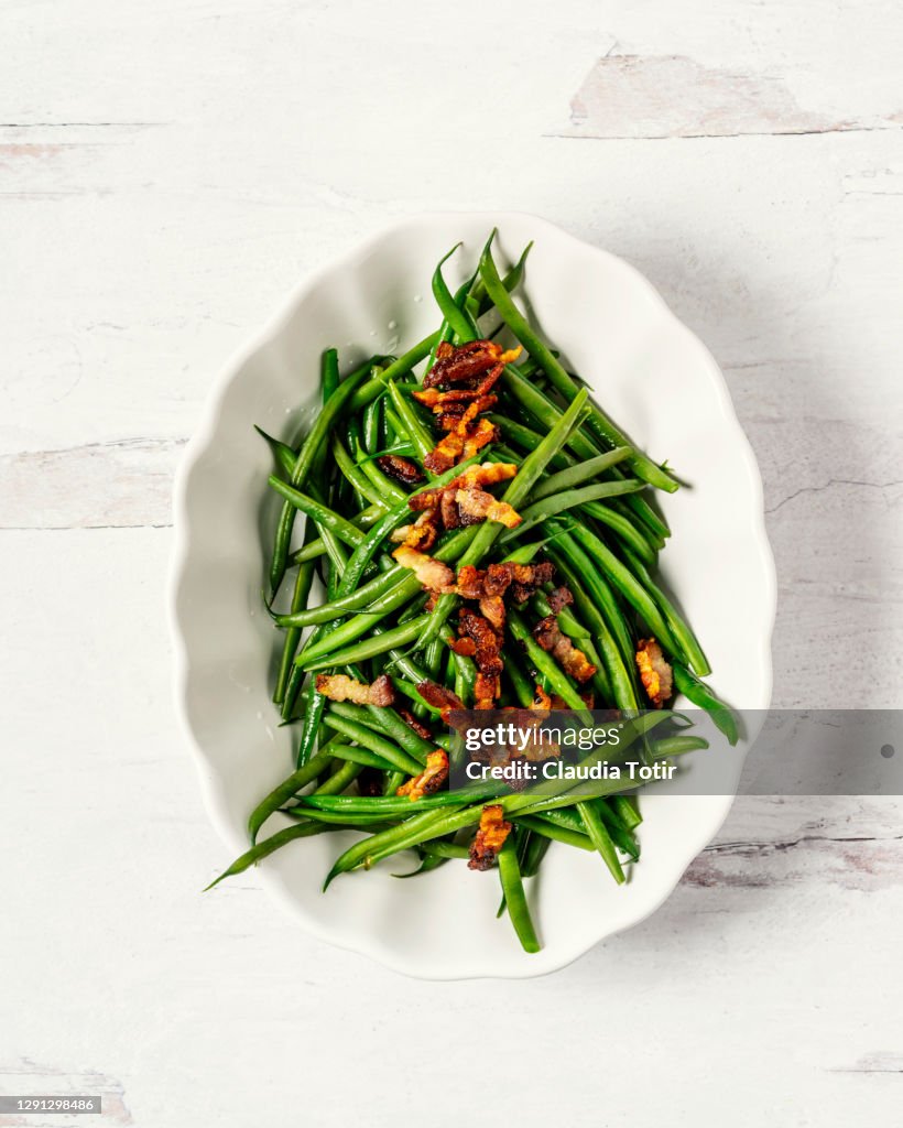 Bowl of green beans with bacon on white, wooden background