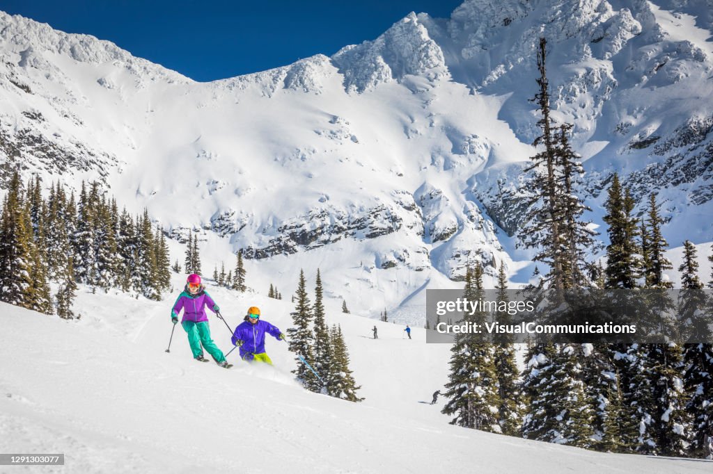 Couple skiing on groomed ski run on sunny day.