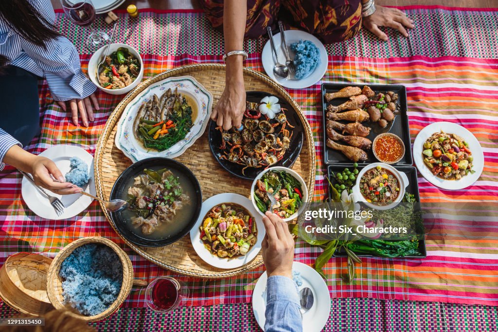 Group of Asian people family enjoy celebrating Thai food dinner while sitting on mat at home, Northeast thailand (Issan) healthy traditional Thai foods concept, Top view