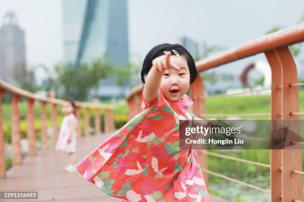 a chinese female kid running towards us when her sister was in the background on a footpath that built upon a water pond in a park - red dress run stock pictures, royalty-free photos & images