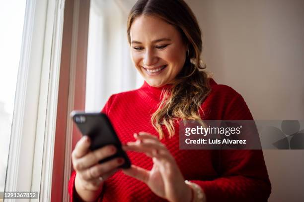 woman texting on her smart phone and smiling - smartphone zuhause stock-fotos und bilder
