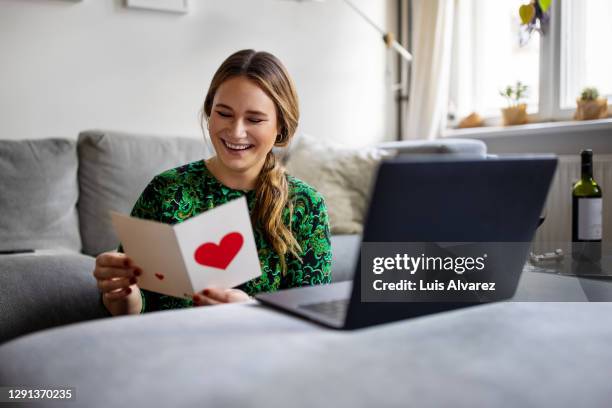 woman reading a greeting card during a video call - lange afstandsrelatie stockfoto's en -beelden