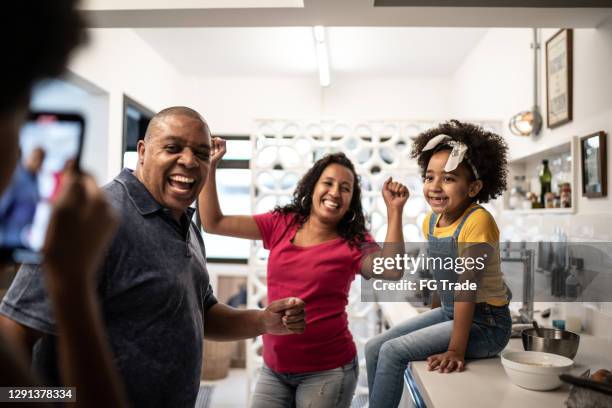 familie tanzt in der küche, während tochter sie zu hause filmt - afro jokes stock-fotos und bilder