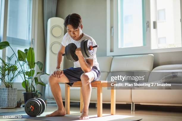 a man lifting dumbbell at home - musculation des biceps photos et images de collection