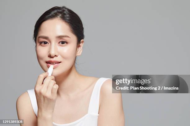 a woman putting lip balm on lips - dry lips stock pictures, royalty-free photos & images