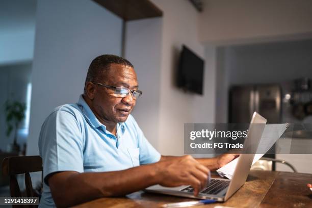 hombre de la tercera edad pagando facturas o haciendo finanzas domésticas - old man afro fotografías e imágenes de stock