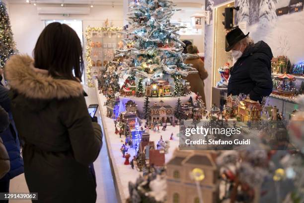 People wearing protective masks look inside a Christmas decoration shop on December 15, 2020 in Turin, Italy. Italy is preparing for the holiday...