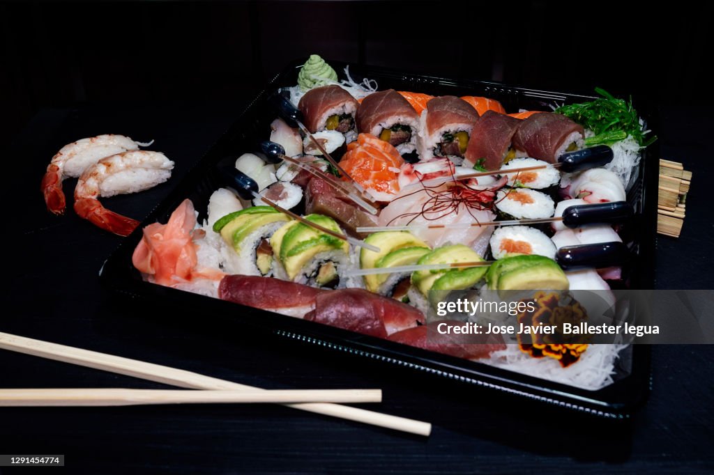 Close-up of a take-away tray with assorted sushi. Nigiri, Maki, Uramaki, Temaki, Oshi, Osomaki, Temari, Futomaki, Gunkan, Jazari, Oshi battera, Inari Dark food