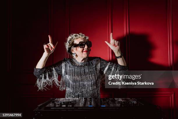 old woman stands with headphones at the dj console and plays music and dances - dança de discoteca imagens e fotografias de stock