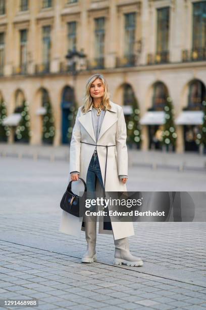 Xenia Adonts wears a golden necklace from Paco Rabanne, a gray wool pullover, a trench coat from Bottega Veneta, blue jeans, a black leather bag from...