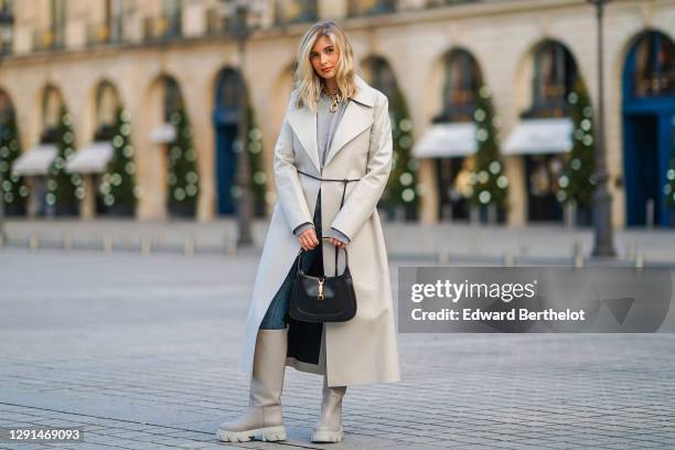 Xenia Adonts wears a golden necklace from Paco Rabanne, a gray wool pullover, a trench coat from Bottega Veneta, blue jeans, a black leather bag from...