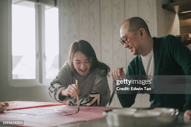 playful asian chinese family having fun drawing father face while writing chinese calligraphy on red paper for prosperity and preparing chinese new year home decoration - caligraphy stock pictures, royalty-free photos & images